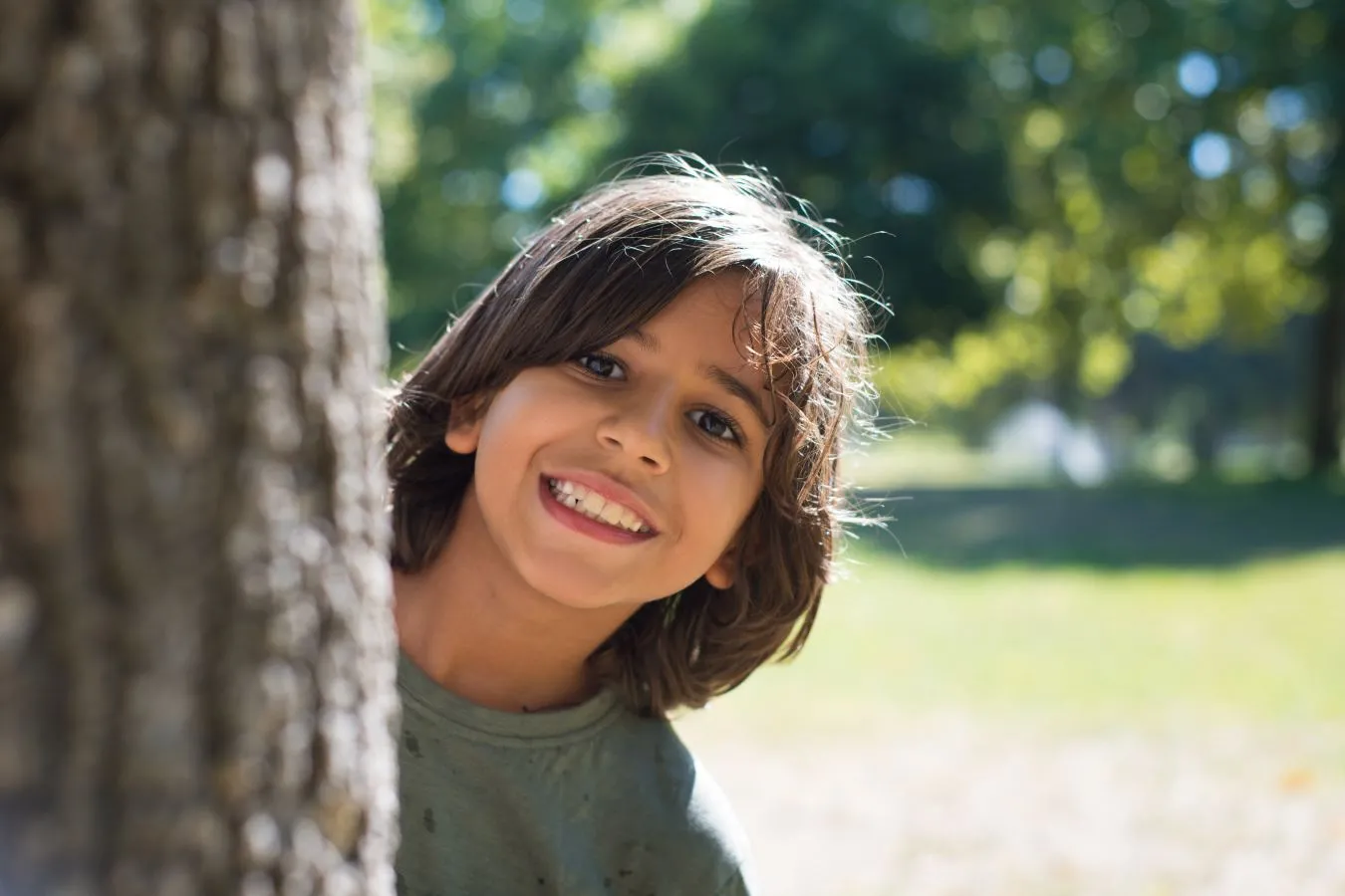 Young boy peering around a tree and smiling