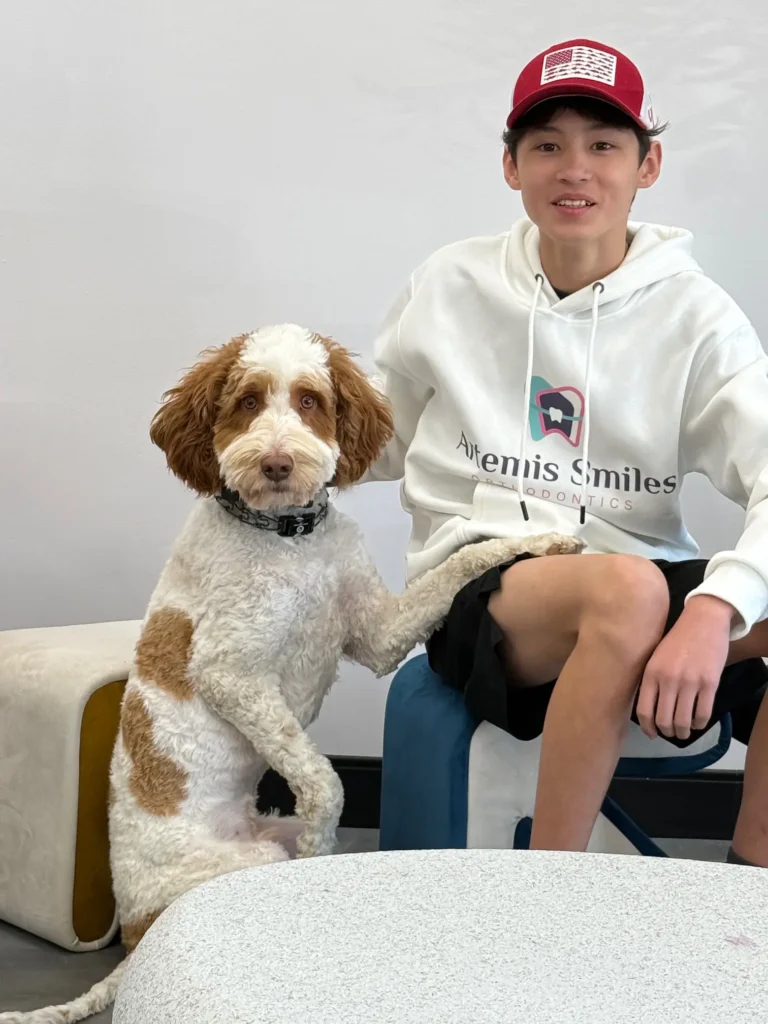 Teen patient in an Artemis Smiles hoodie sitting with the practice therapy dog.