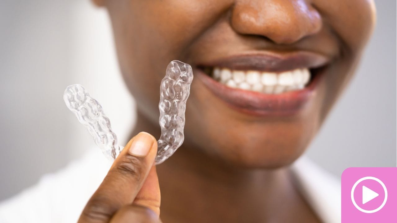 Smiling patient holding a clear aligner tray up beside their teeth.