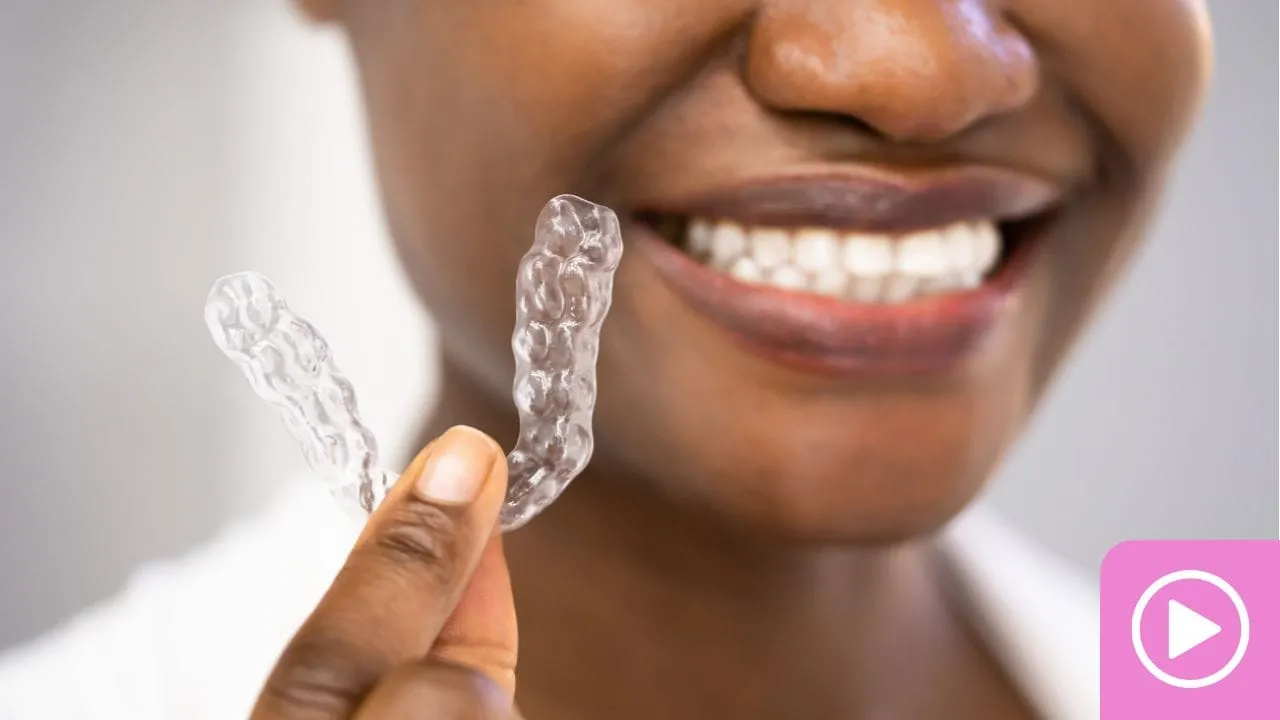 Smiling patient holding a clear aligner tray up beside their teeth.
