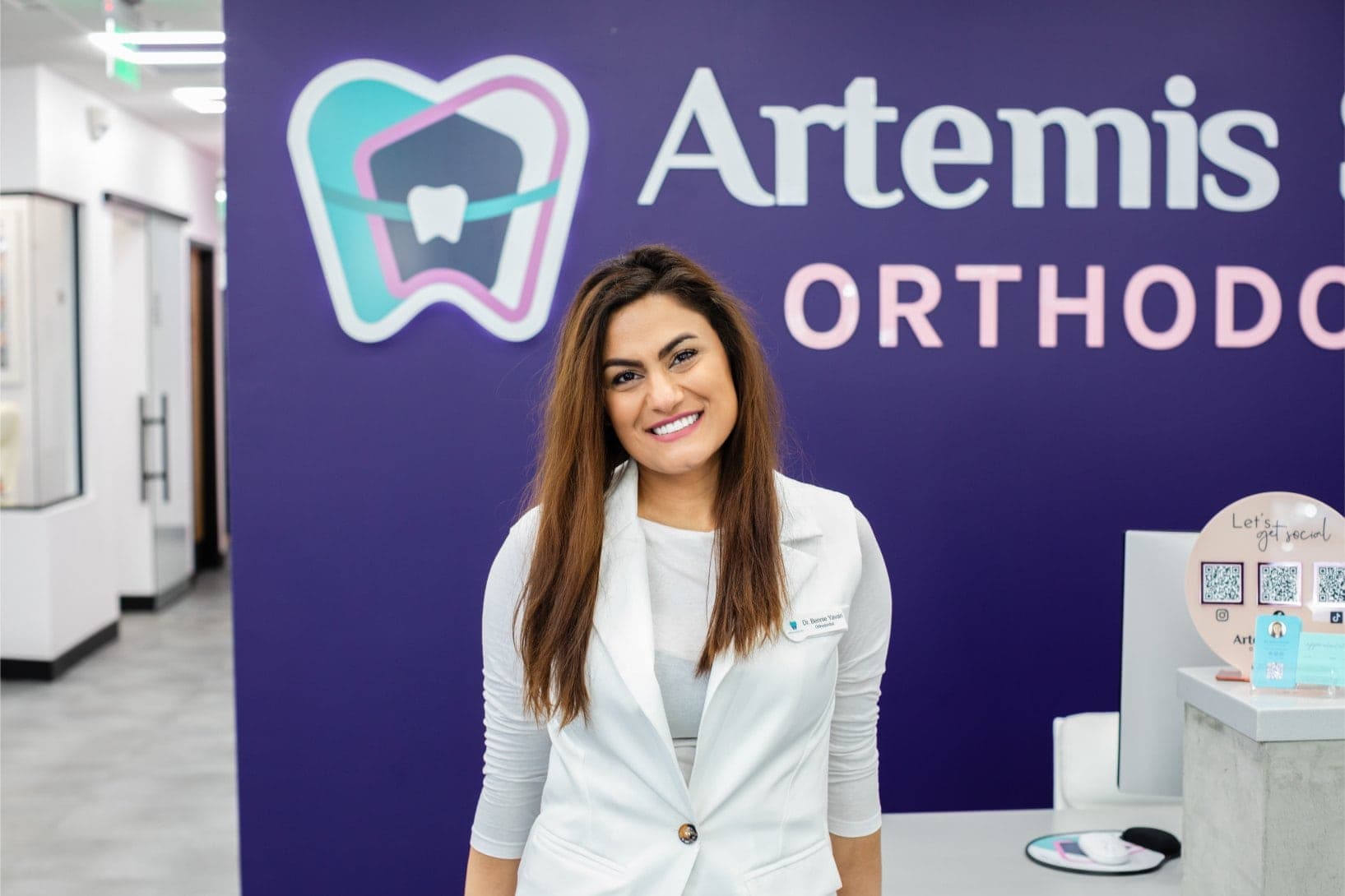 Team member standing beside the Artemis Smiles Orthodontics wall sign